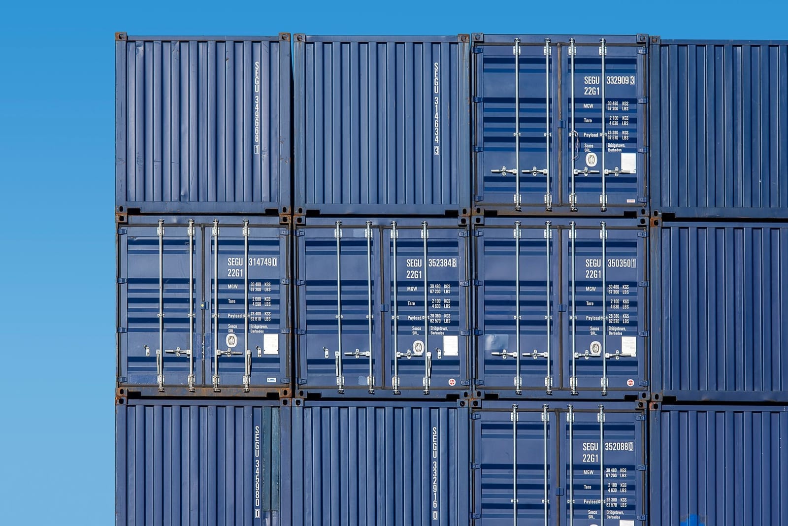 Blue shipping containers stacked high in a port storage yard, representing cargo sitting idle while demurrage and detention charges accrue
