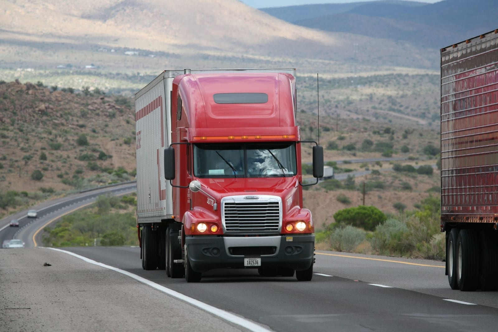 Loaded semi-truck travelling along an open highway, representing road freight moving containerised cargo from the port to the factory door
