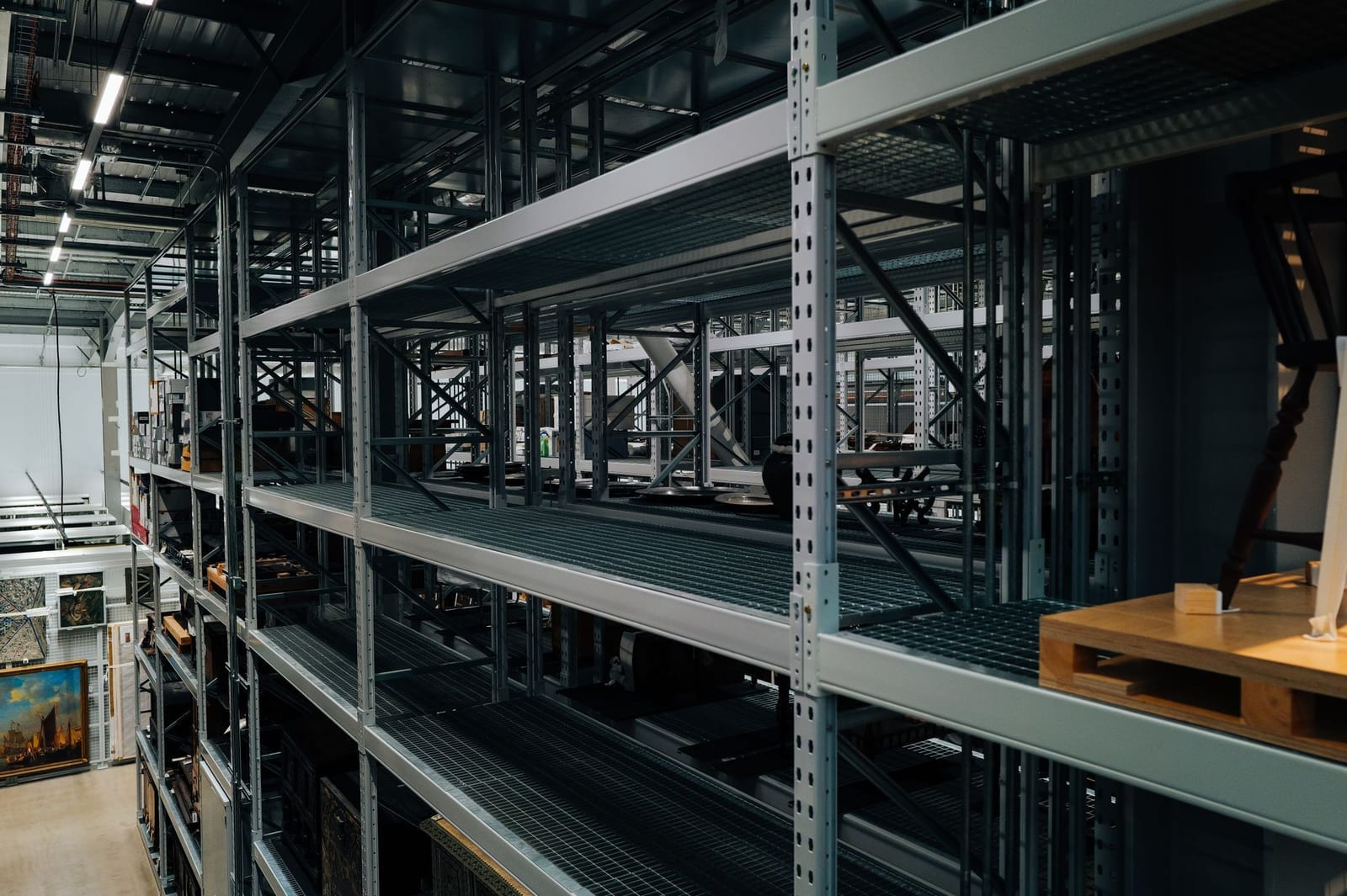 Rows of empty metal storage racks inside a spacious industrial warehouse, representing warehousing and distribution capacity for imported goods